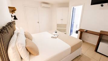 Quarto de hotel com cama, escrivaninha, televisão e guarda-roupa.