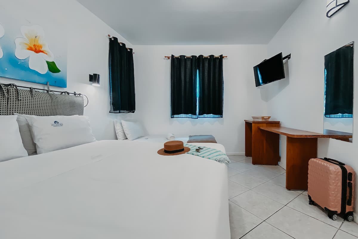 Quarto de hotel com cama, escrivaninha, televisão e mala.