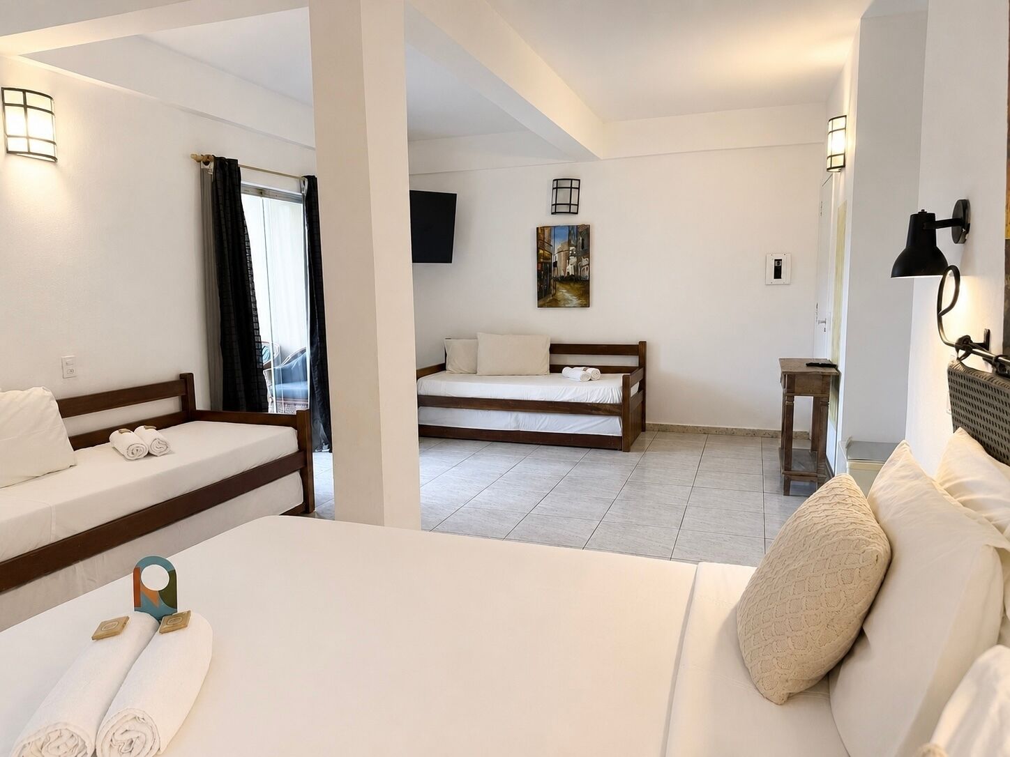 A hotel room with two beds, a television, a painting, and a lamp.