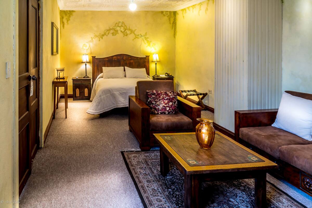 Una habitación de hotel con una cama, dos mesitas de noche, una silla, un sofá y una mesa de centro.