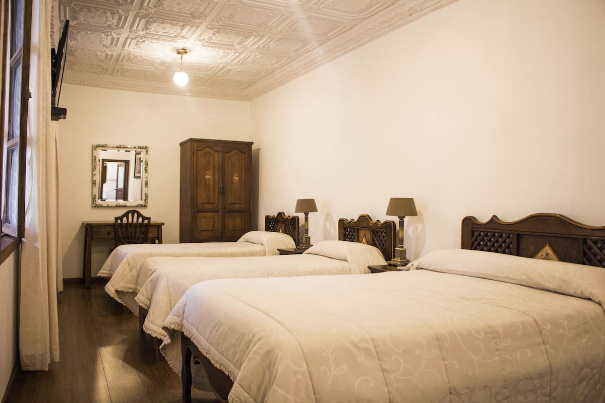 Una habitación de hotel con dos camas individuales, un armario de madera, un escritorio con silla y un espejo en la pared.