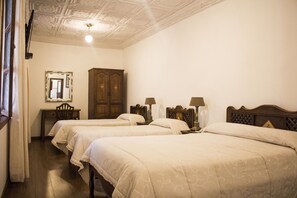 Una habitación de hotel con dos camas individuales, un armario de madera, un escritorio con silla y un espejo en la pared.