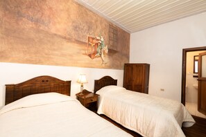 Un dormitorio con dos camas, cabeceros de madera, una mesita de noche con una lámpara y un mural grande en la pared.