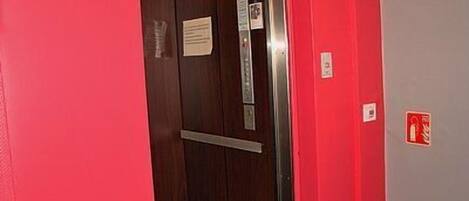Un ascenseur avec un intérieur en bois et un mur rouge à côté.