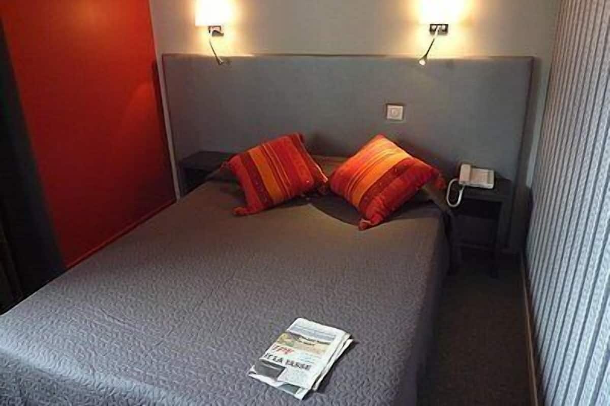 A hotel room with a bed, two nightstands, and two wall-mounted lamps.