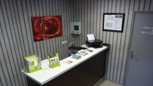 A reception desk with a white counter, a red abstract painting on the wall, a framed notice, and a door labeled "RESTAURANT" and "PETIT OVEN".