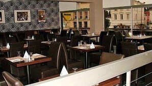 A restaurant with tables and chairs arranged in rows, a patterned wall, and a view of buildings outside.