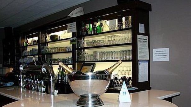 A bar area with a round white counter, a large silver bowl, and shelves stocked with bottles and glasses.