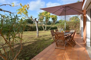 An outdoor patio with a table and chairs, surrounded by a garden with various plants and trees. - Les Belles Ombres (Cargese)