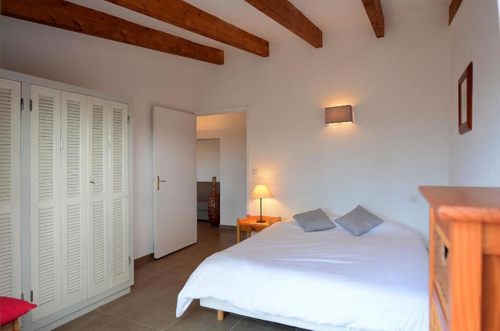 Une chambre à coucher comprenant un lit, une table de chevet, une lampe, une armoire et une poutre en bois au plafond.