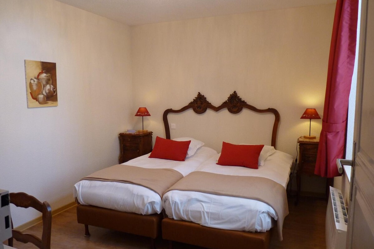A double bed with two pillows, a wooden headboard, bedside tables with lamps, a chair, and a painting on the wall.