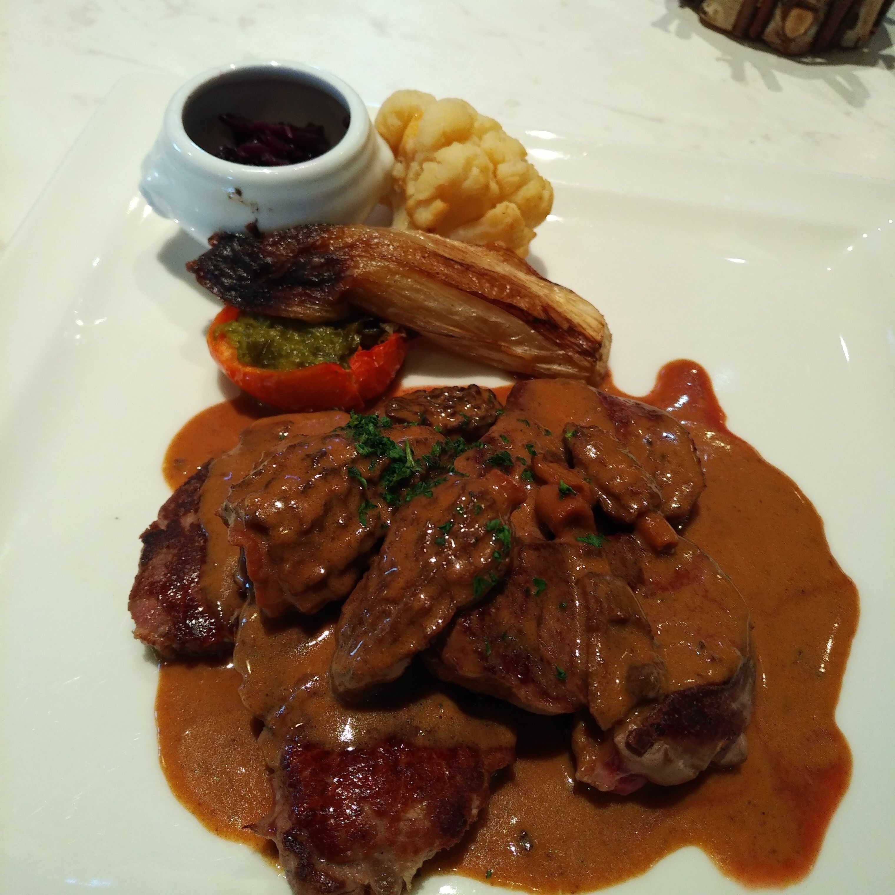 A plate of food with steak, vegetables, and a sauce.