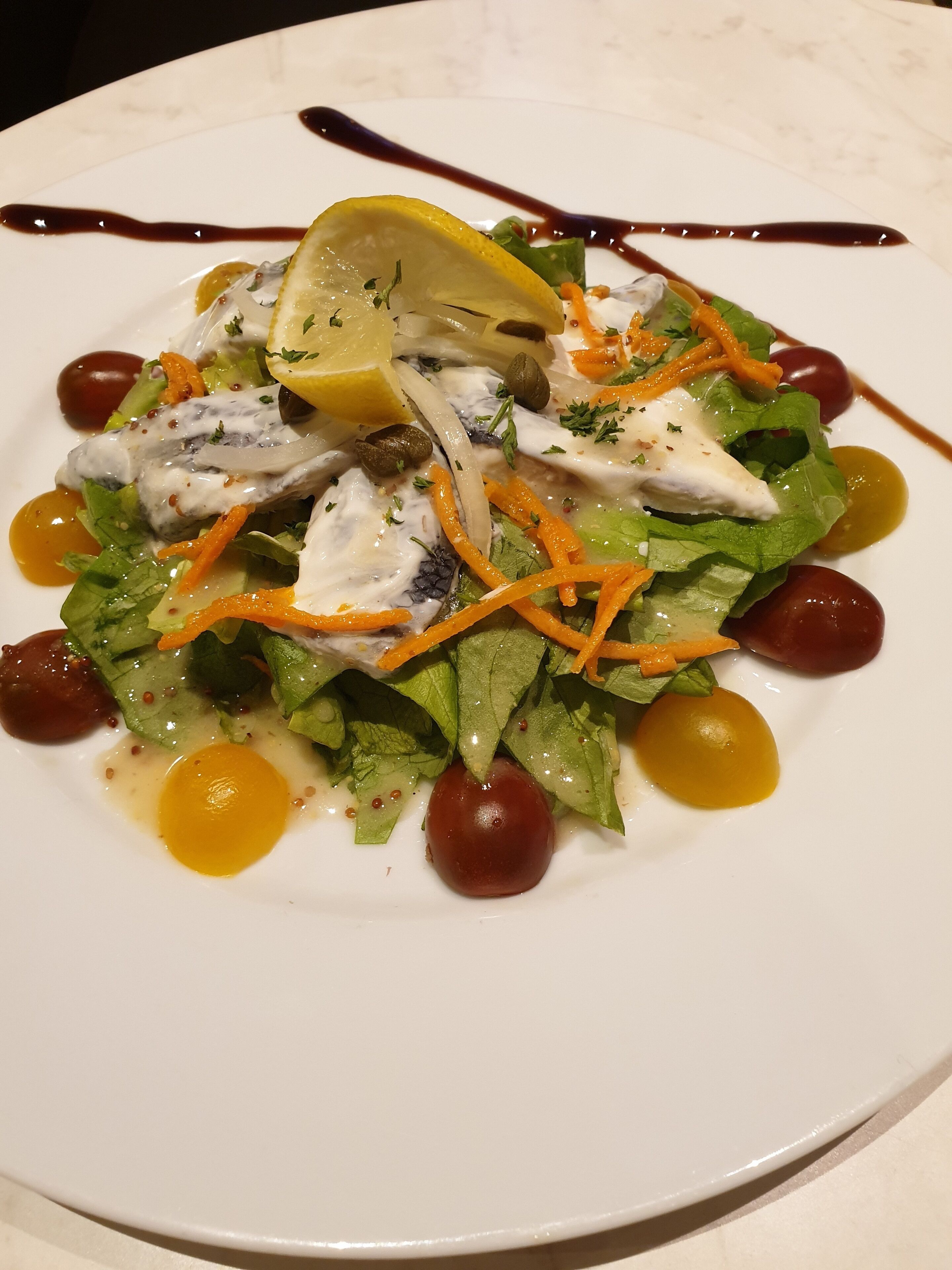Un plato blanco con una ensalada de lechuga, tomates cherry y una rodaja de limón.