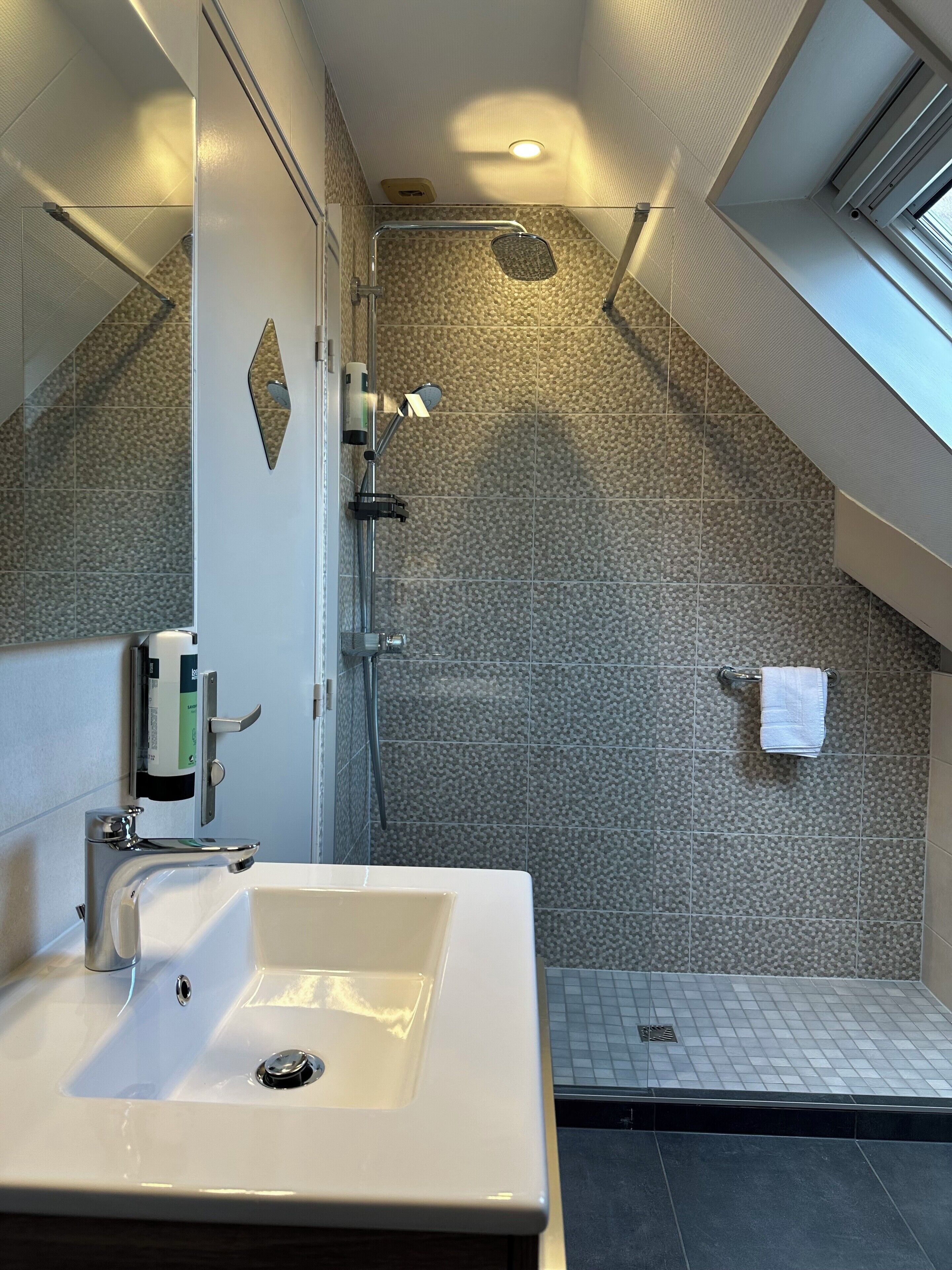 A modern bathroom with a large sink, a shower, and a towel rack.