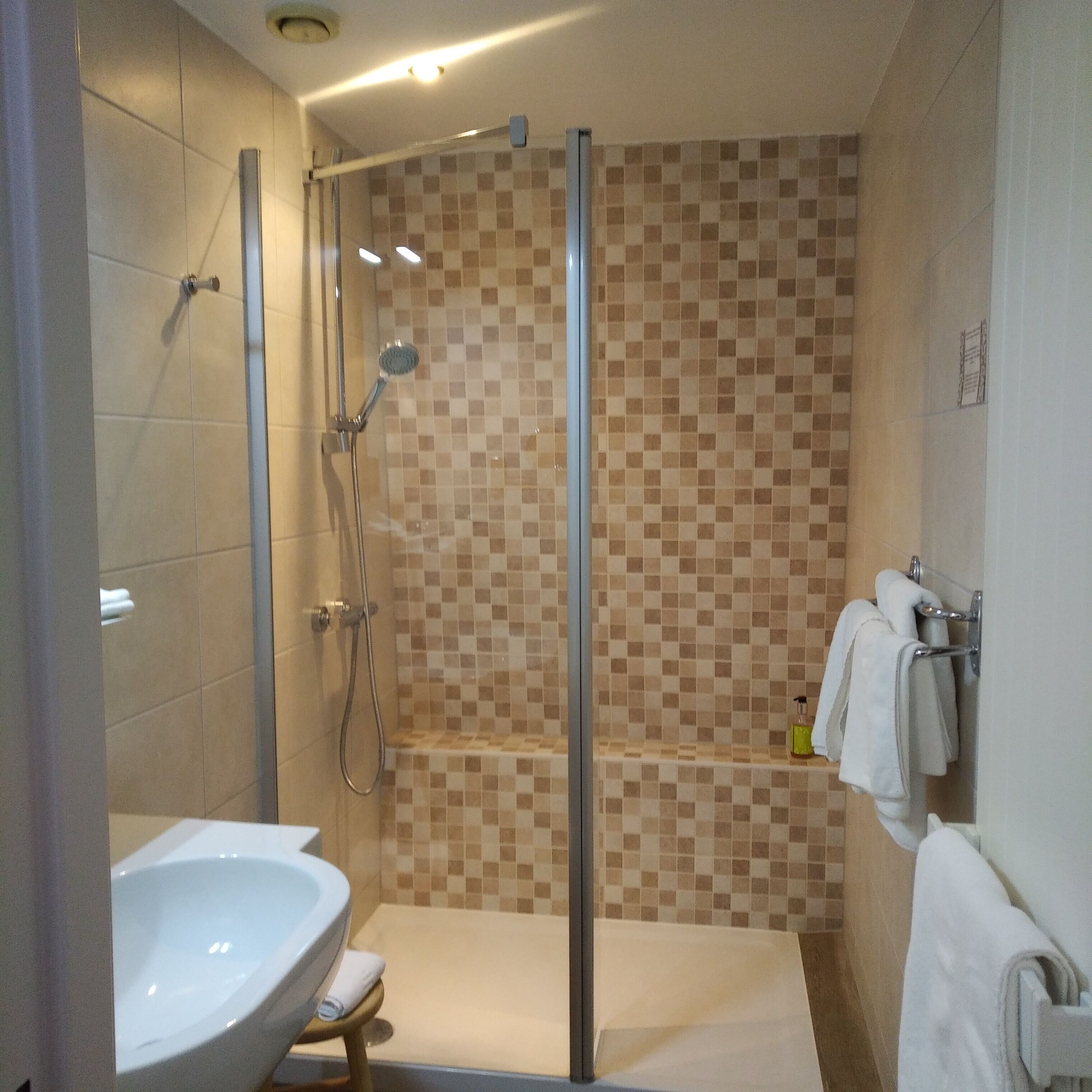 Ein modernes Badezimmer mit Duschkabine aus Glas, einem weißen Waschbecken und einer gefliesten Duschwand.