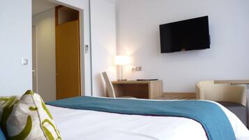 Une chambre d’hôtel avec un lit, un bureau, une chaise, une télévision et une porte.