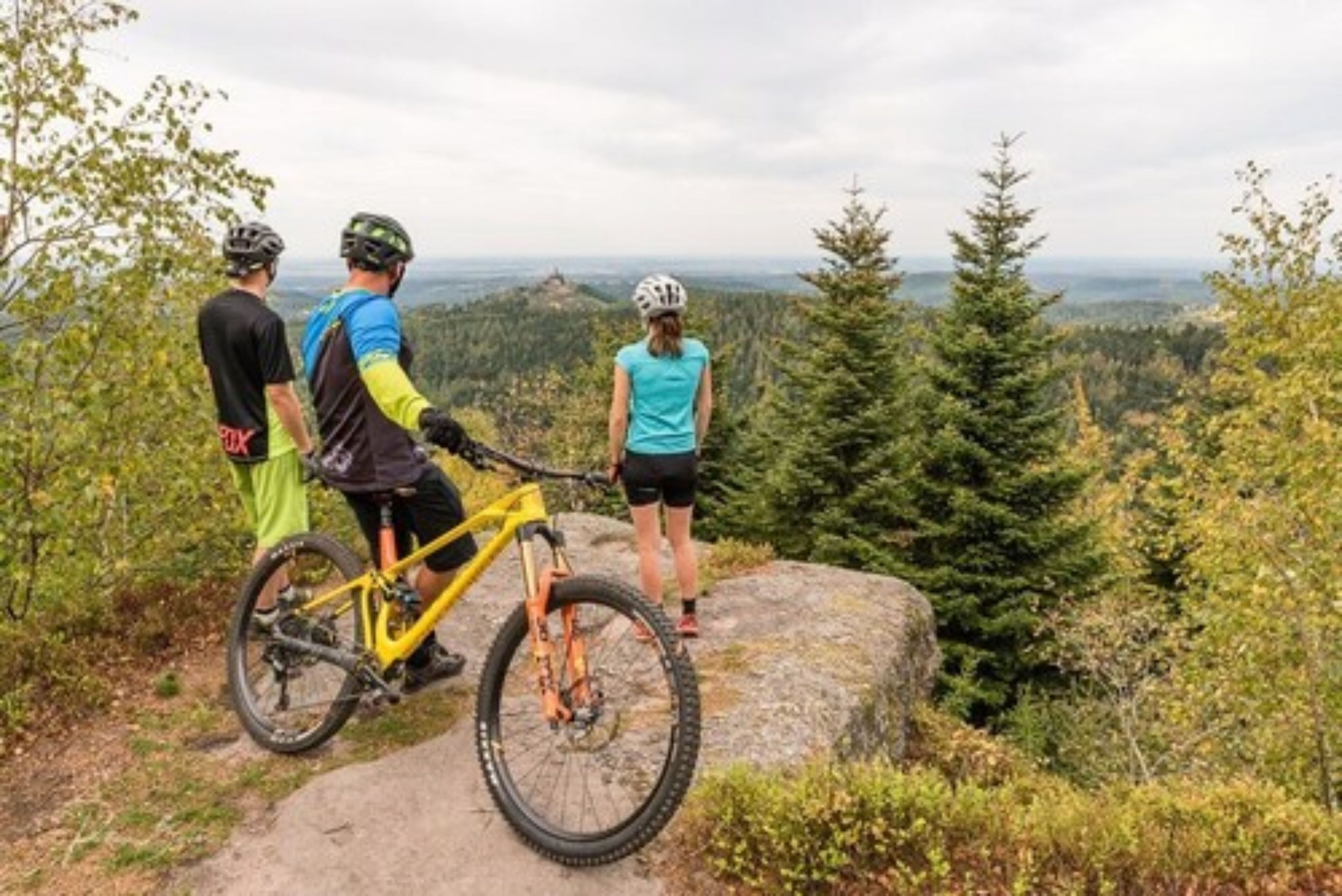 Tres personas de pie sobre un afloramiento rocoso, con vistas a la montaña.