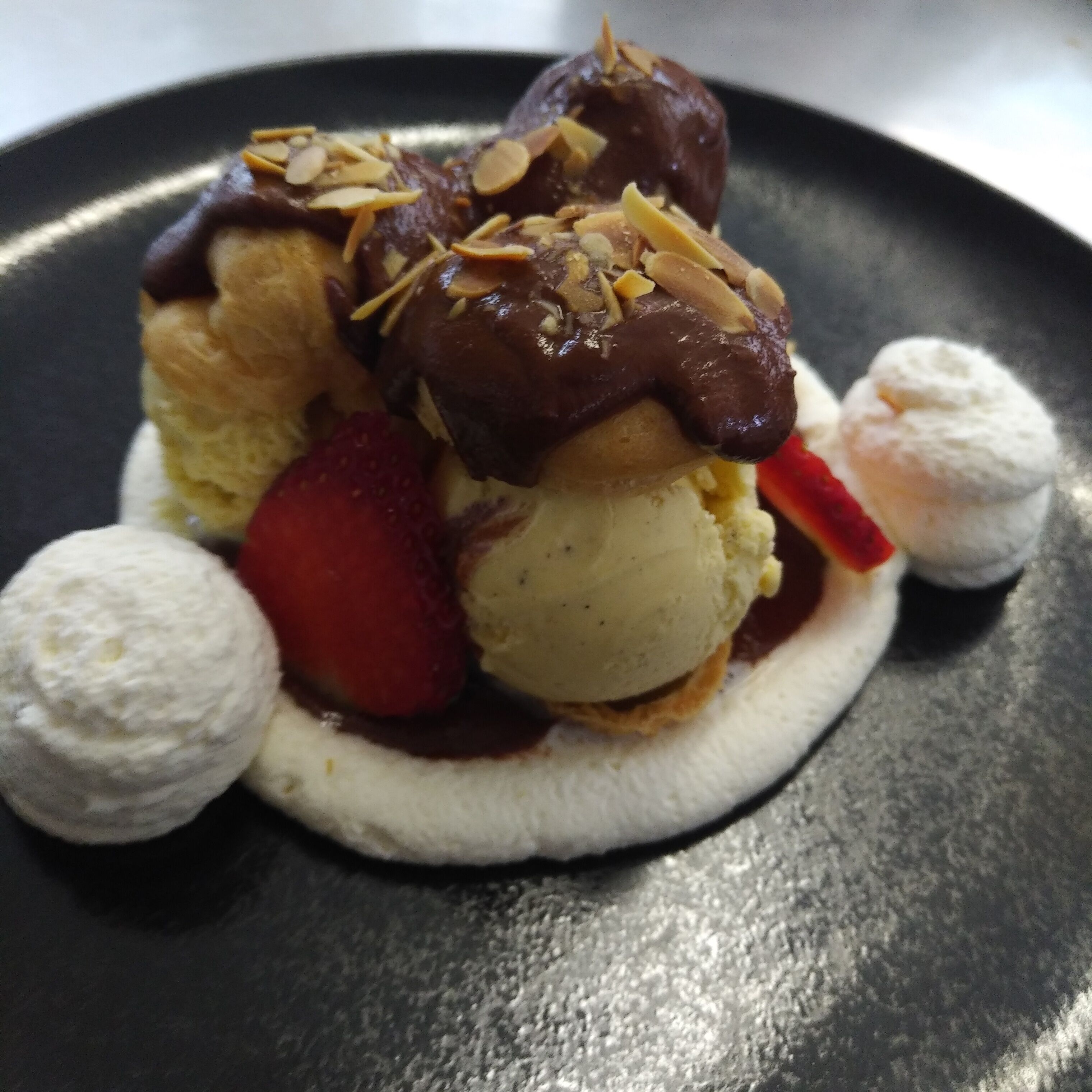 A dessert with ice cream, strawberries, and almonds on a plate.