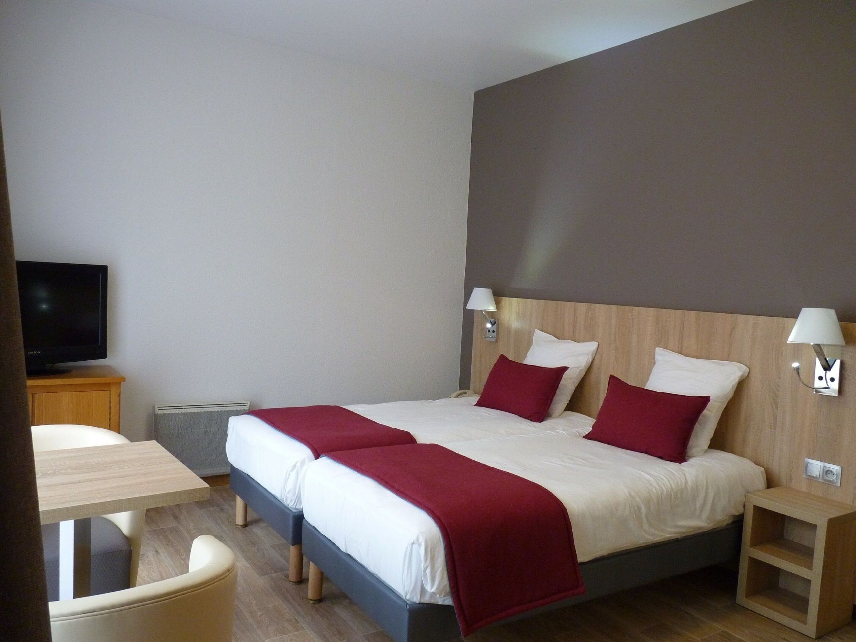 Une chambre d’hôtel avec un grand lit, deux tables de chevet, une télévision et une petite table avec des chaises.
