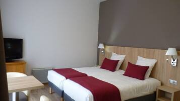 Habitación de hotel con una cama grande, dos mesitas de noche, un televisor y una pequeña mesa con sillas.