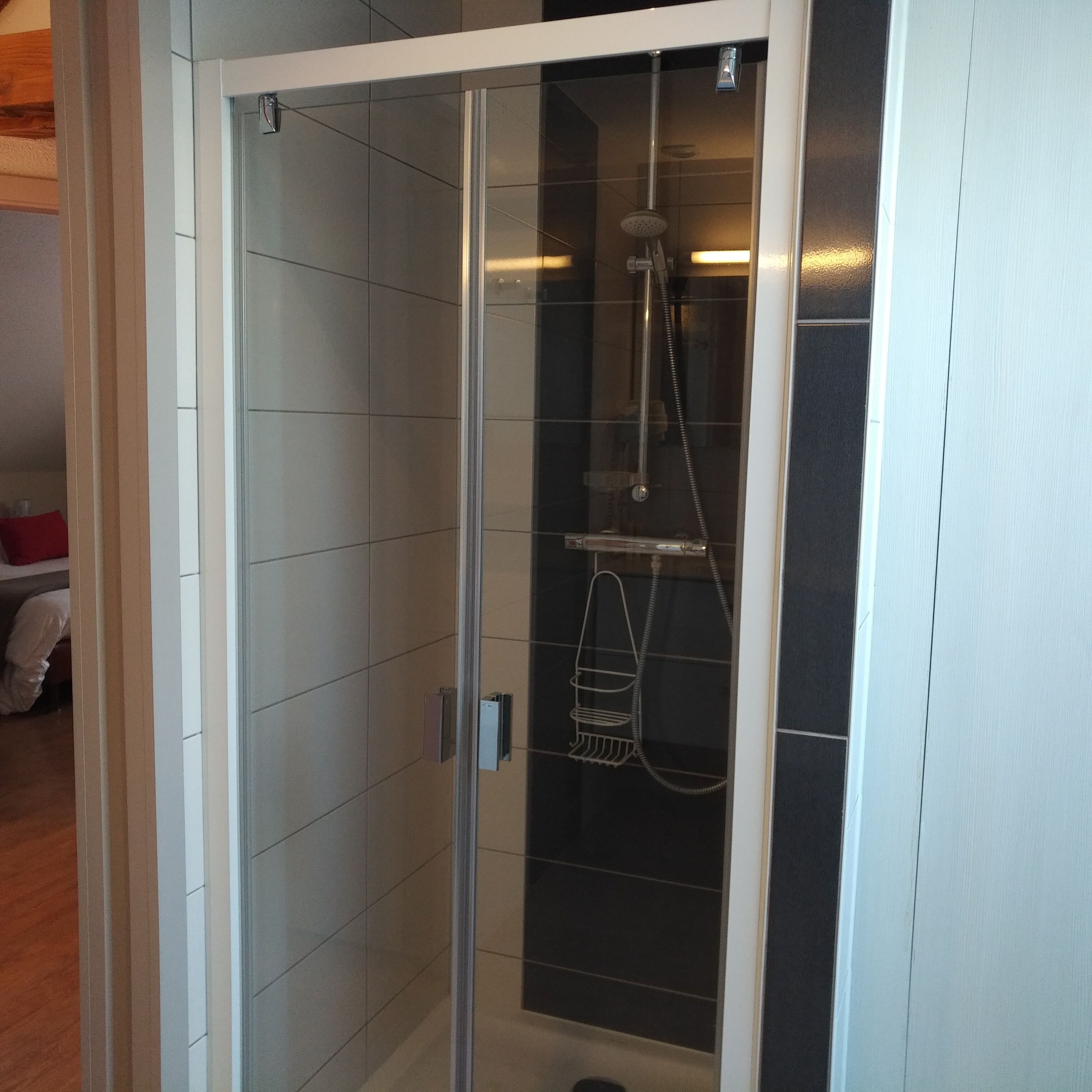A glass-enclosed shower with a handheld showerhead and a wall-mounted faucet.