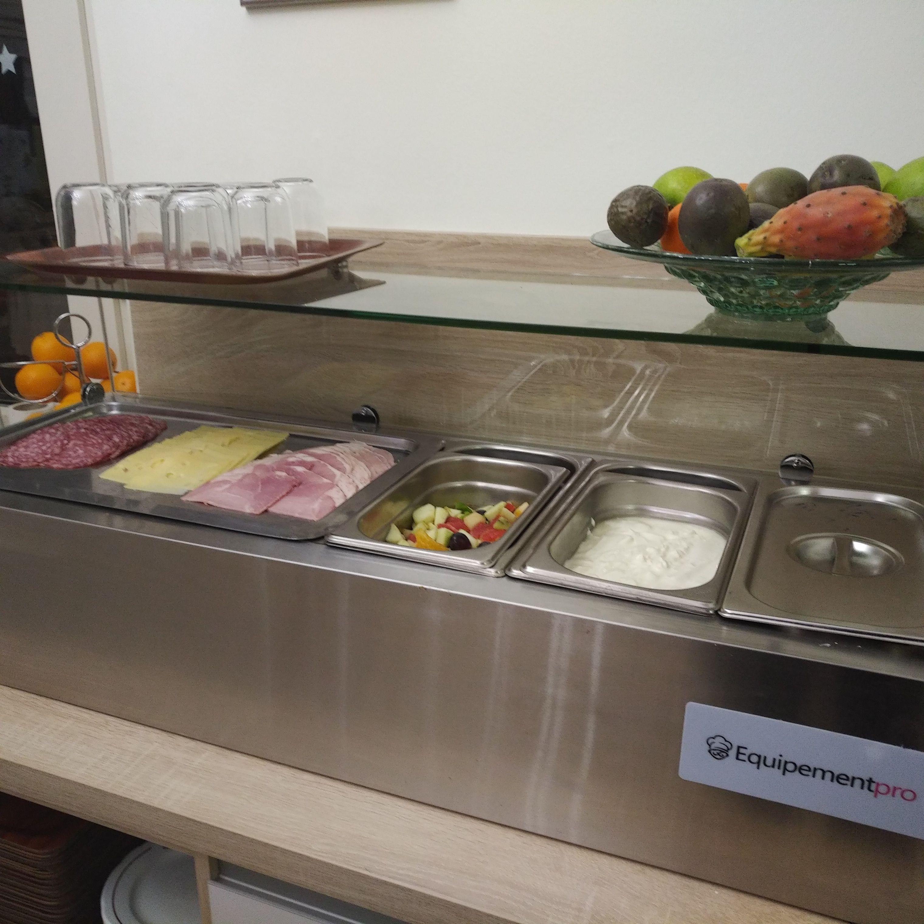 Zona de bufé con diversas opciones de comida, incluyendo carnes, quesos, frutas y un plato de yogur.