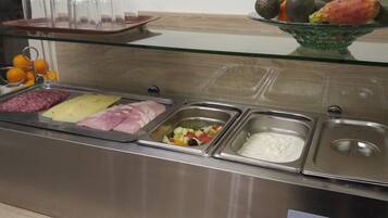 Zona de bufé con diversas opciones de comida, incluyendo carnes, quesos, frutas y un plato de yogur.