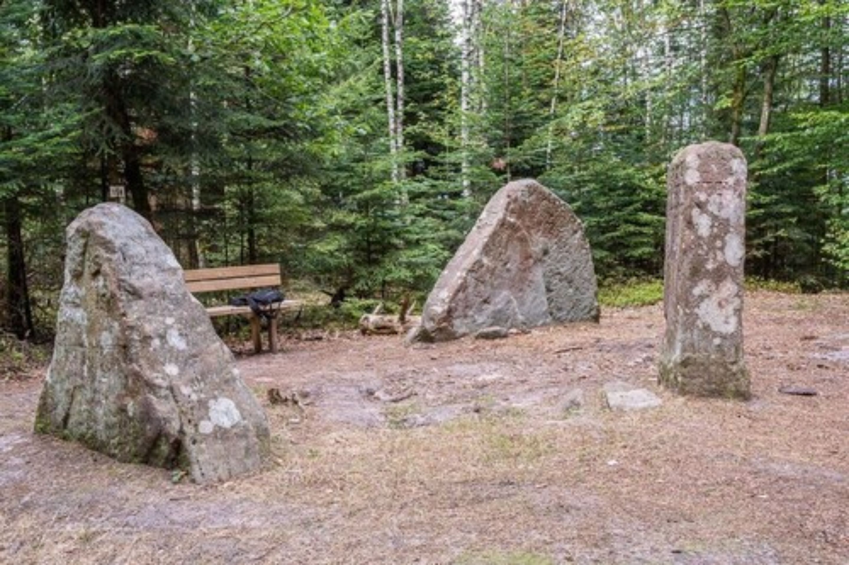 A forested area with three large boulders and a wooden bench.