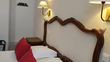 A hotel room with a wooden headboard, two bedside lamps, a bed with white and red bedding, and a small bedside table.