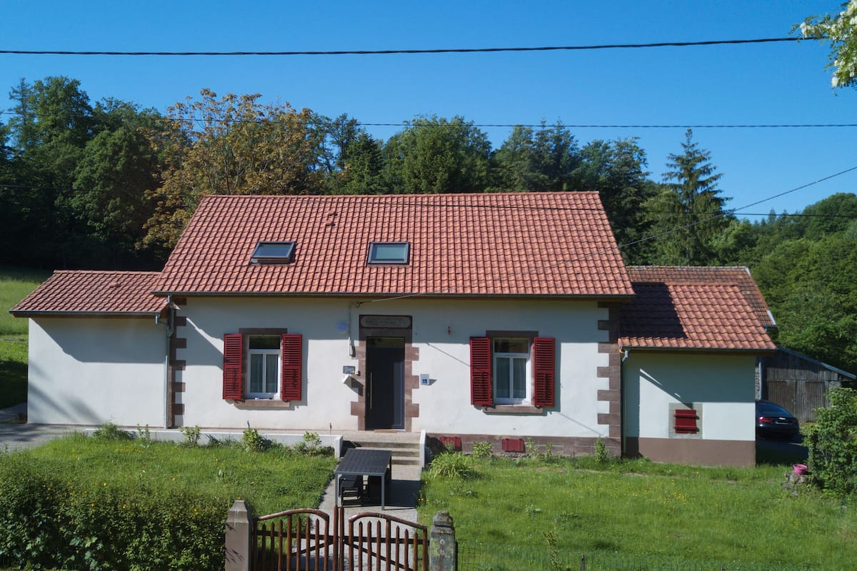 A two-story house with a red-tiled roof, a small front porch, and a paved driveway.