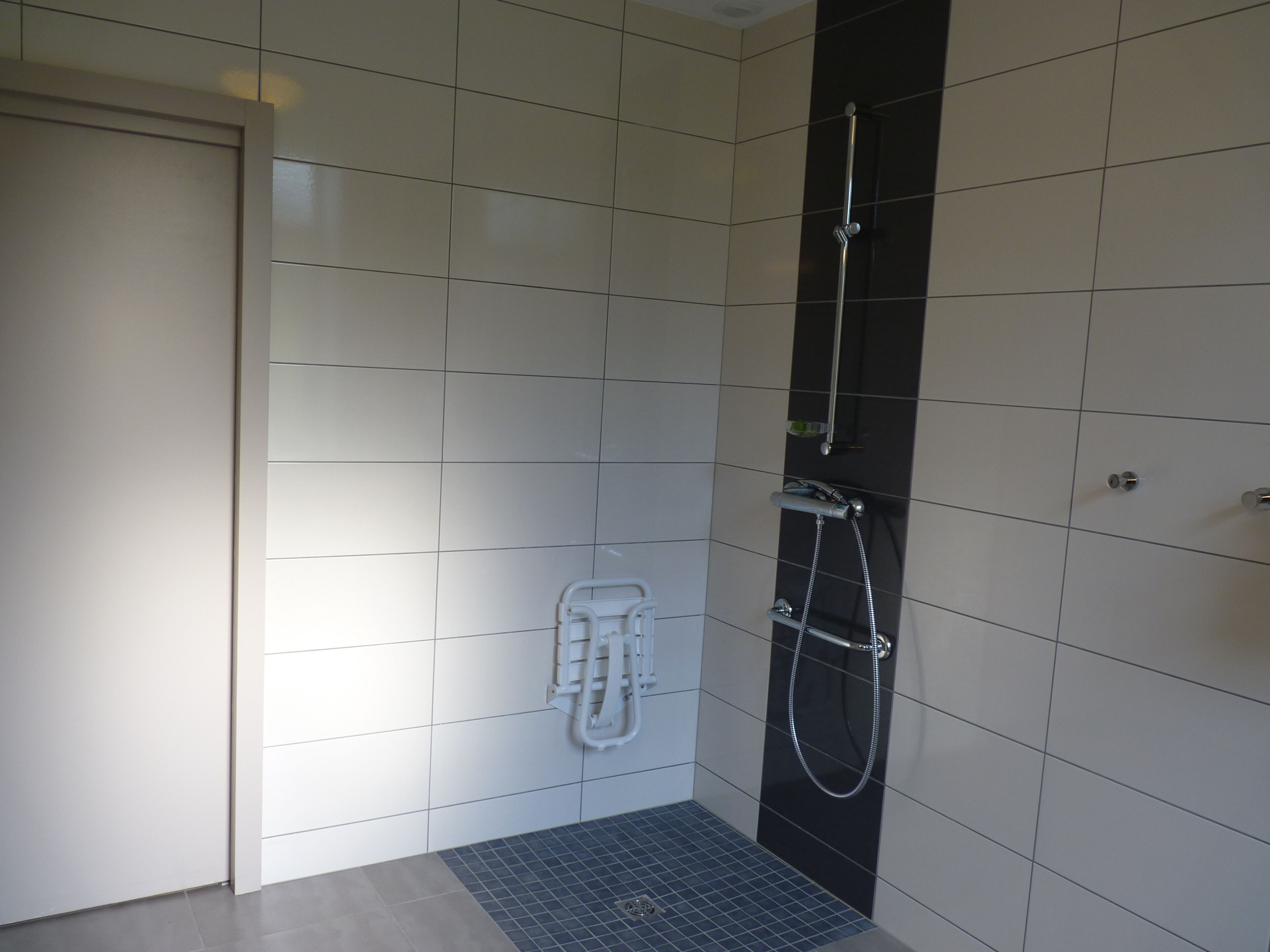 A modern bathroom with white and black tiled walls, a shower with a handheld showerhead, and a small step leading to the shower area.