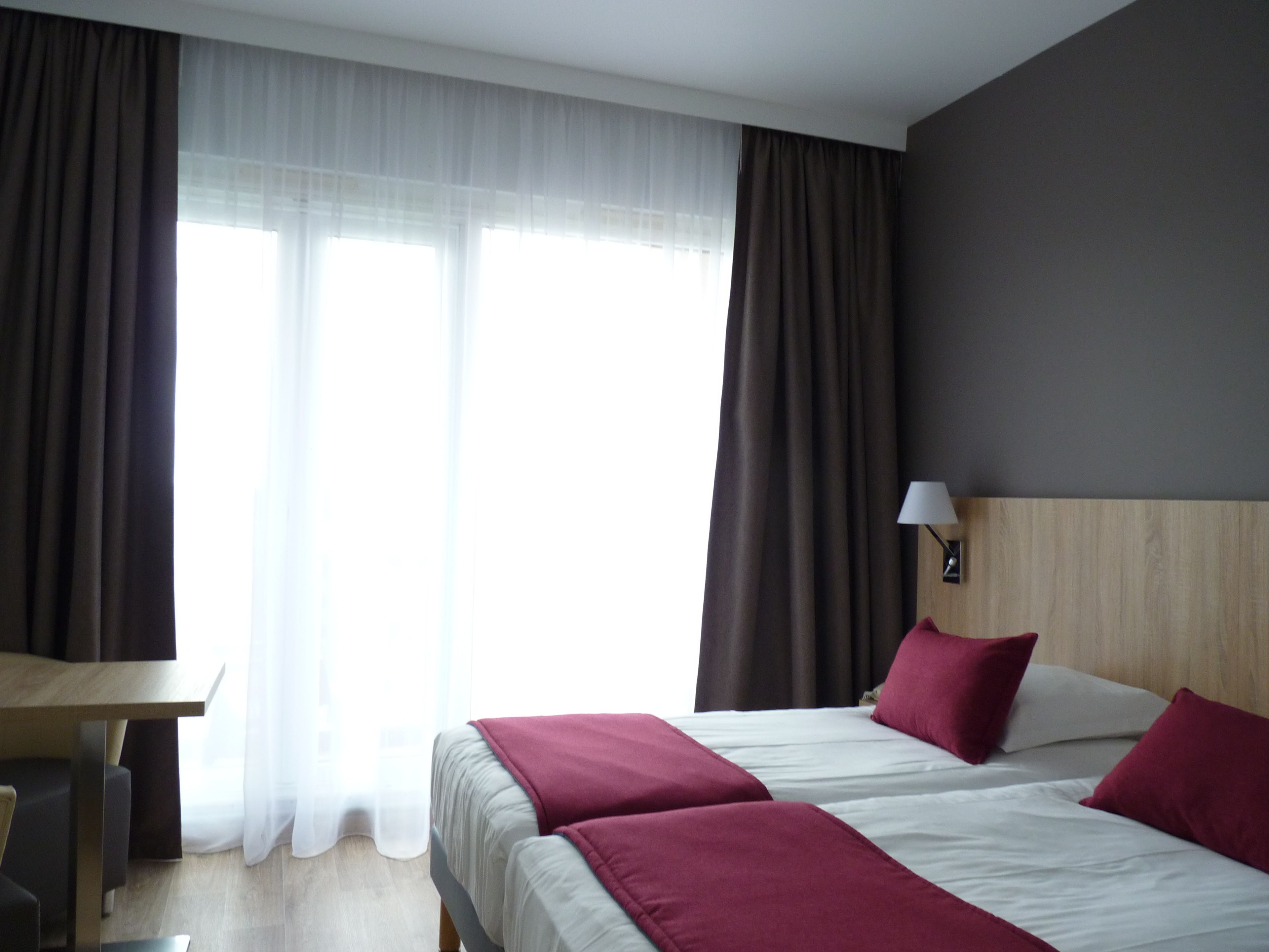 A hotel room with two beds, a desk, and a lamp.