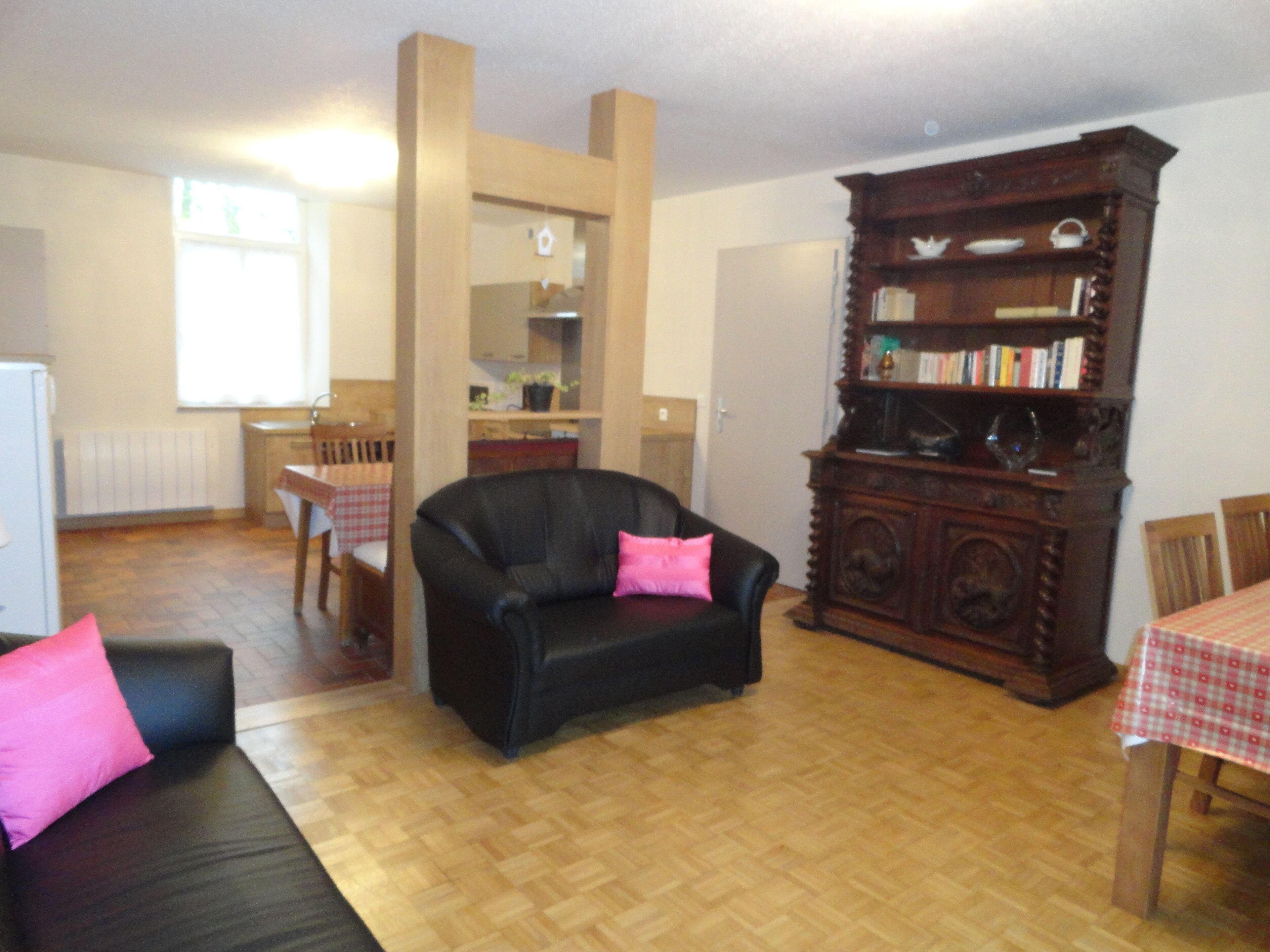 A living room with a black leather sofa, a wooden cabinet, and a dining table with a checkered tablecloth.