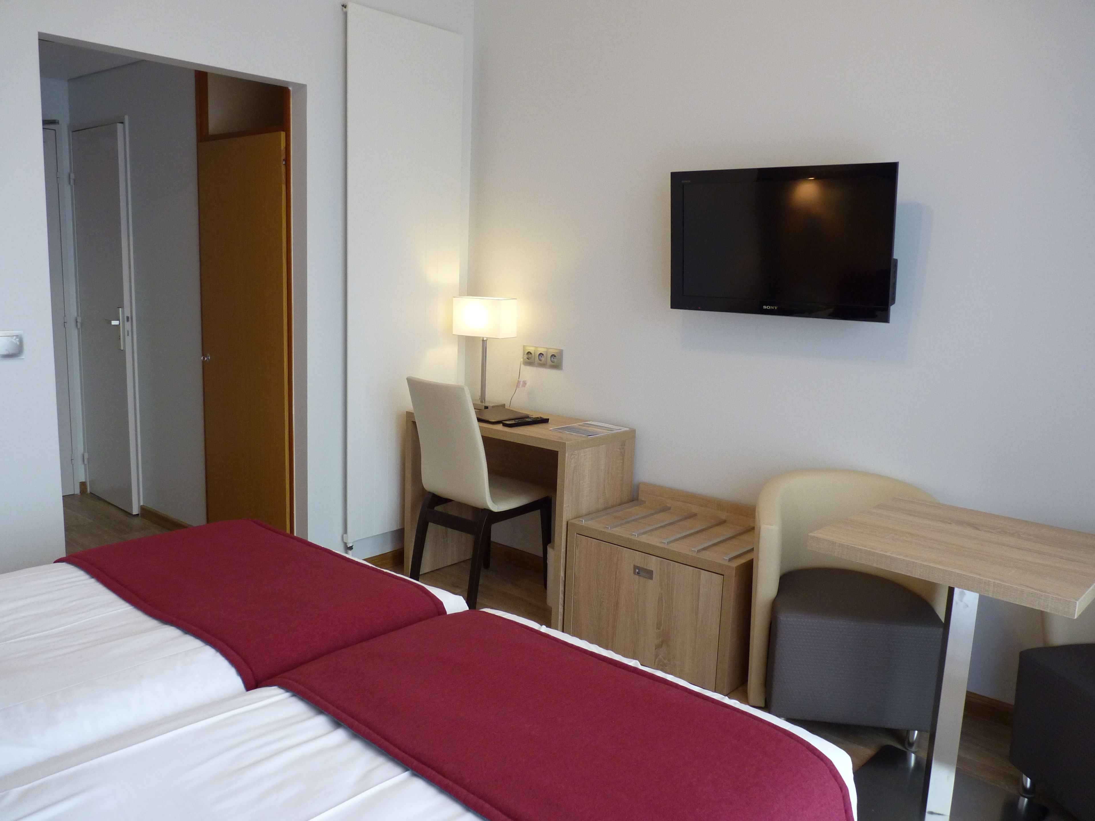 A hotel room with a bed, a desk, a chair, a TV, and a wardrobe.
