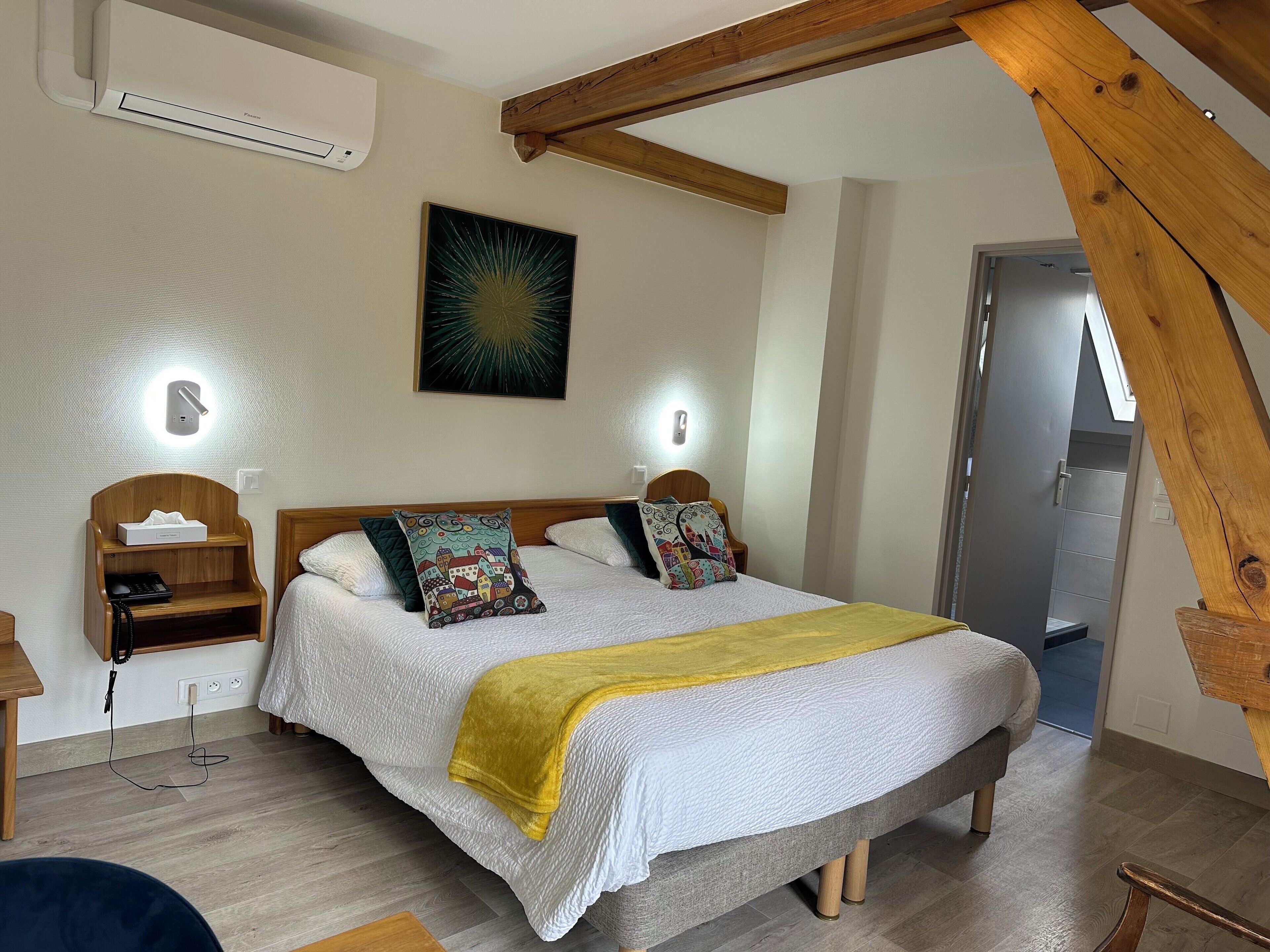 A bedroom with a bed, bedside tables, a bedside lamp, a wall-mounted air conditioner, and a door leading to another room.