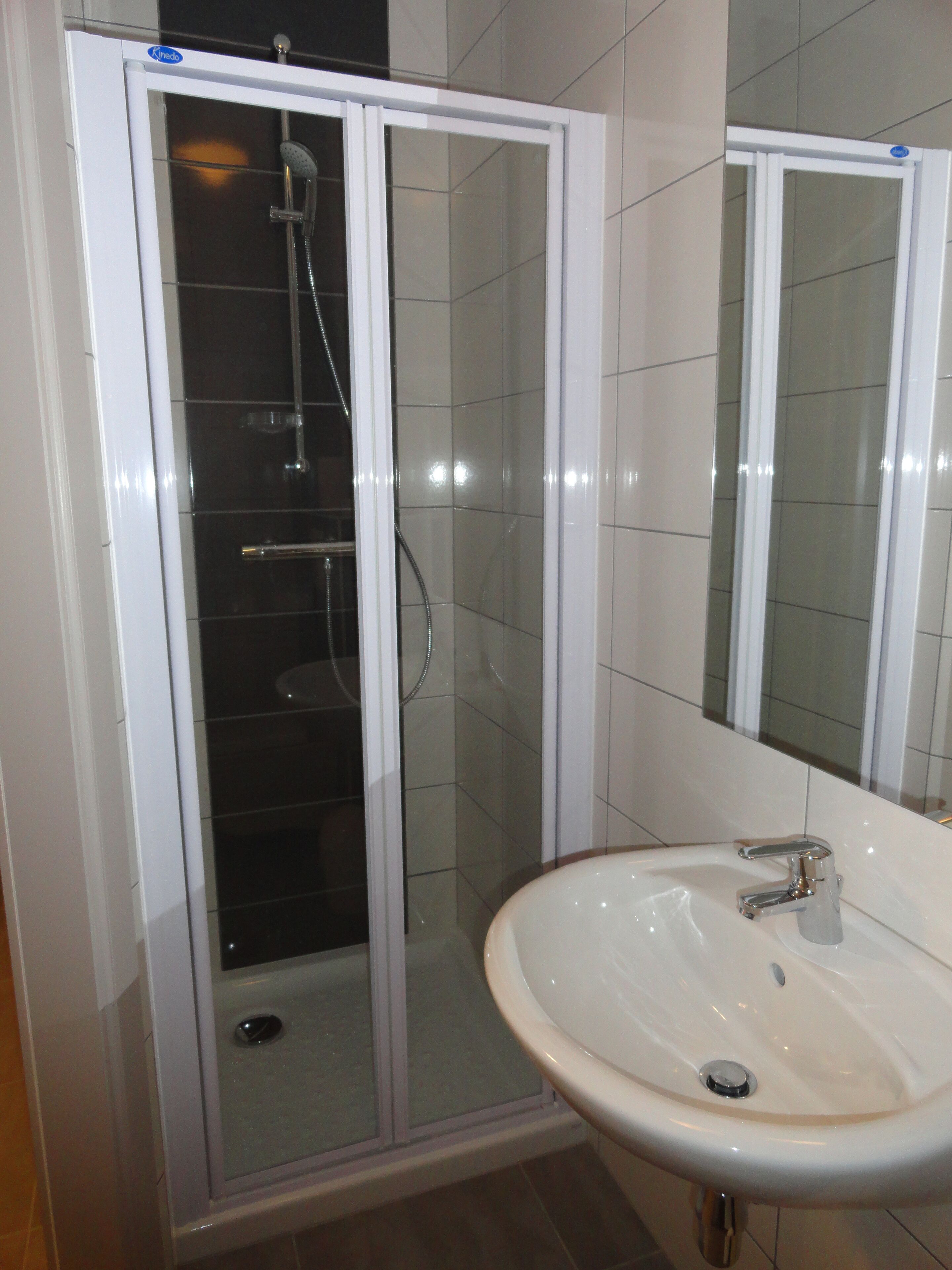 Un baño con ducha vidriada, lavamanos y espejo.