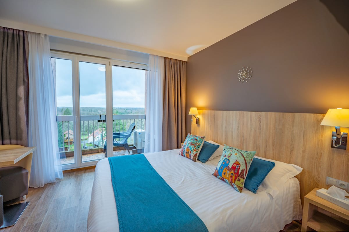 A hotel room with a large bed, a desk, and a view of the outdoors.