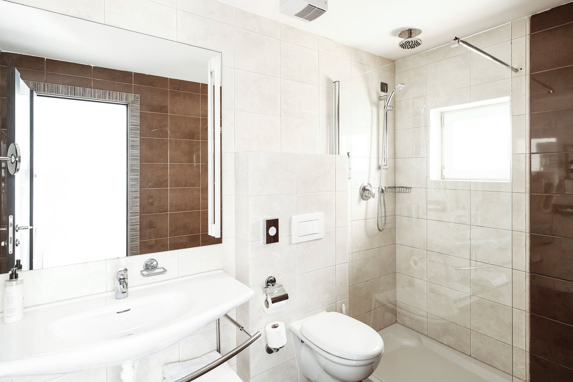 Une salle de bain moderne avec un lavabo blanc, un miroir et des toilettes, un espace douche et une fenêtre.