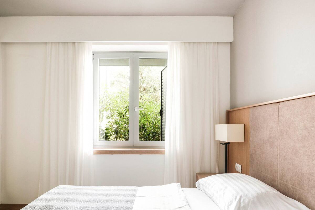 A hotel room with a bed, a nightstand, a lamp, and a window with curtains.