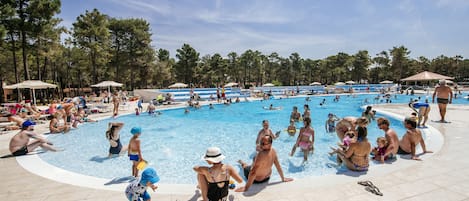 A large outdoor swimming pool surrounded by trees and umbrellas.