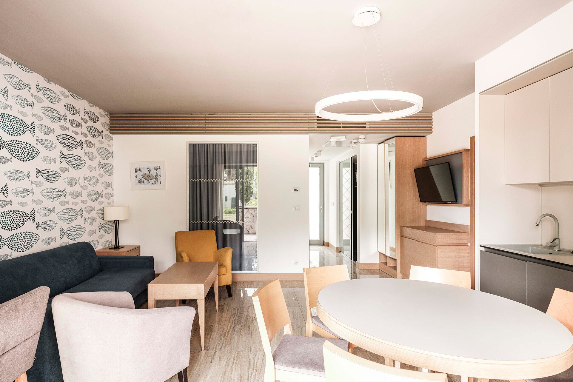 Una sala de estar moderna con un sofá, sillas, una mesa y un televisor montado en un mueble de madera.