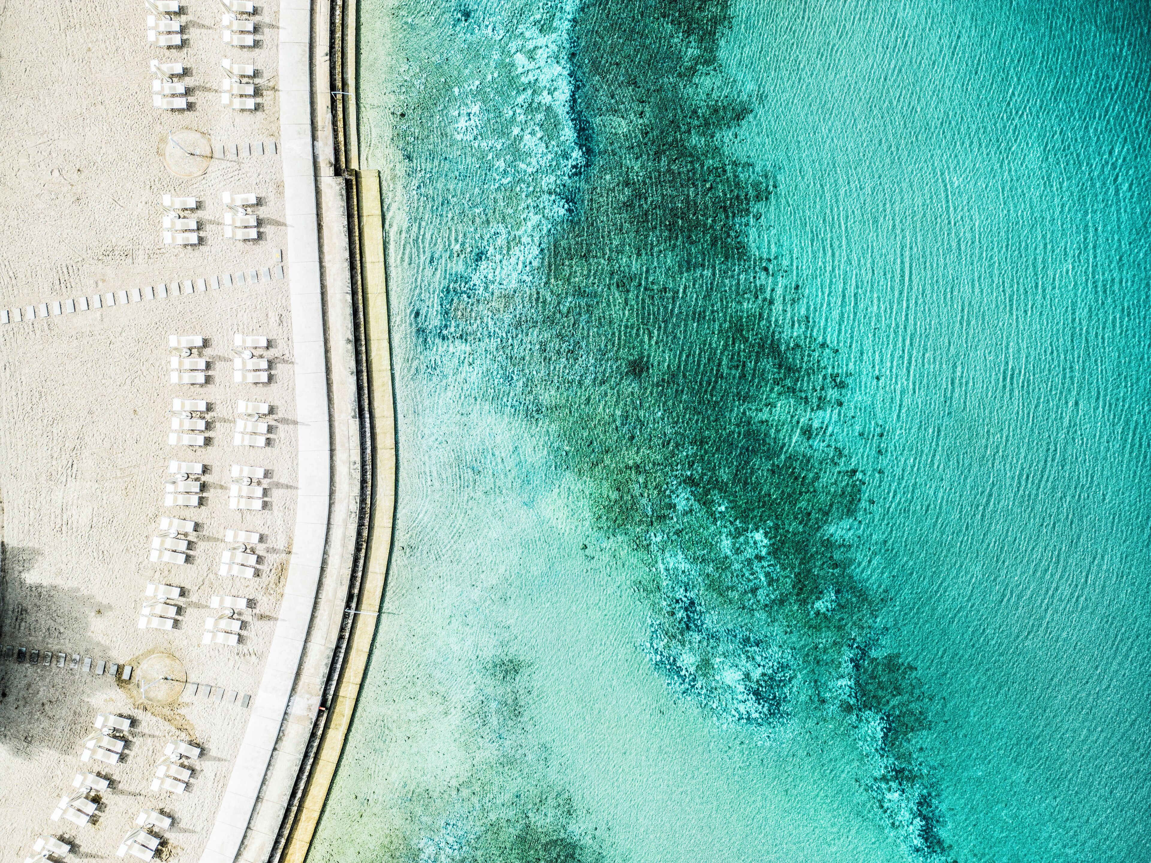 An aerial view of a beach with rows of white sun loungers and a sandy shoreline.