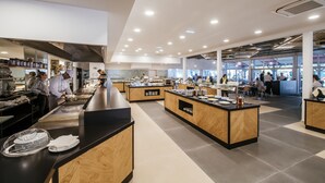 A modern restaurant with multiple dining areas, a central counter, and a kitchen in the background. - Zaton Holiday Resort Apartments (Nin)
