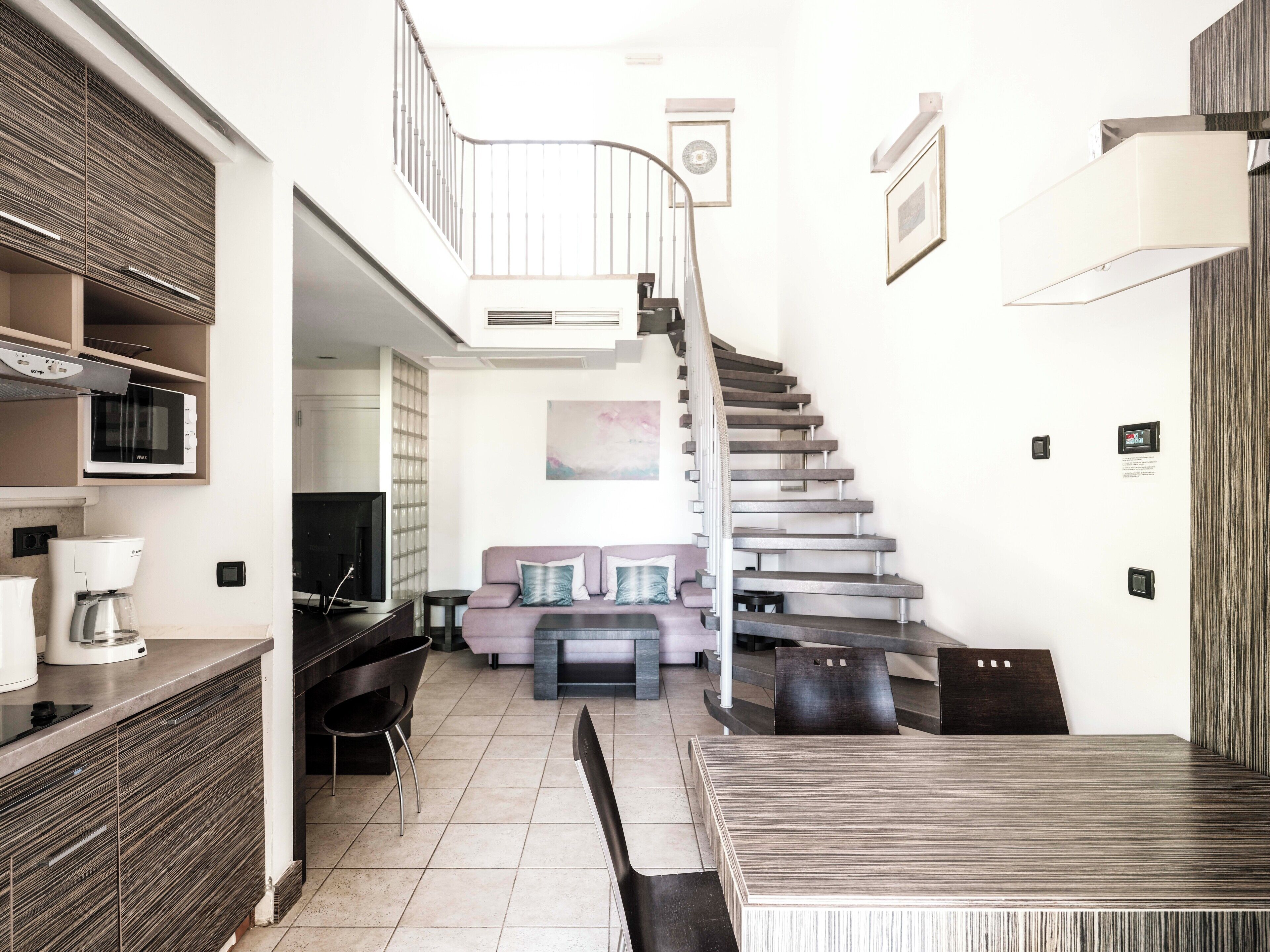 A modern living space with a staircase, a sofa, a dining table, and a kitchen area.
