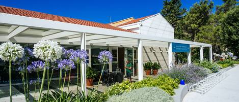 Un espace extérieur abrité, doté d’un toit blanc, de plantes en pot et d’un panneau indiquant l’emplacement de la réception.