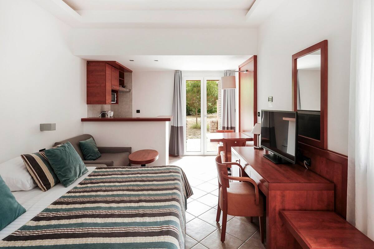 A hotel room with a bed, a sofa, a desk with a TV, and a view of the outdoors.