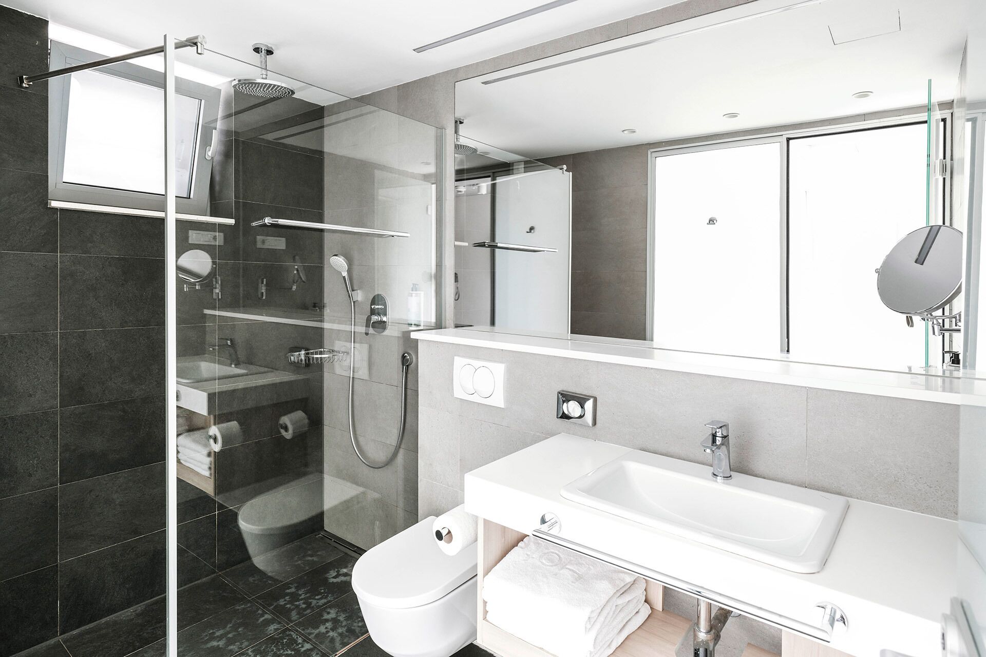 Un baño moderno con ducha de vidrio, un lavabo blanco y un espejo grande.