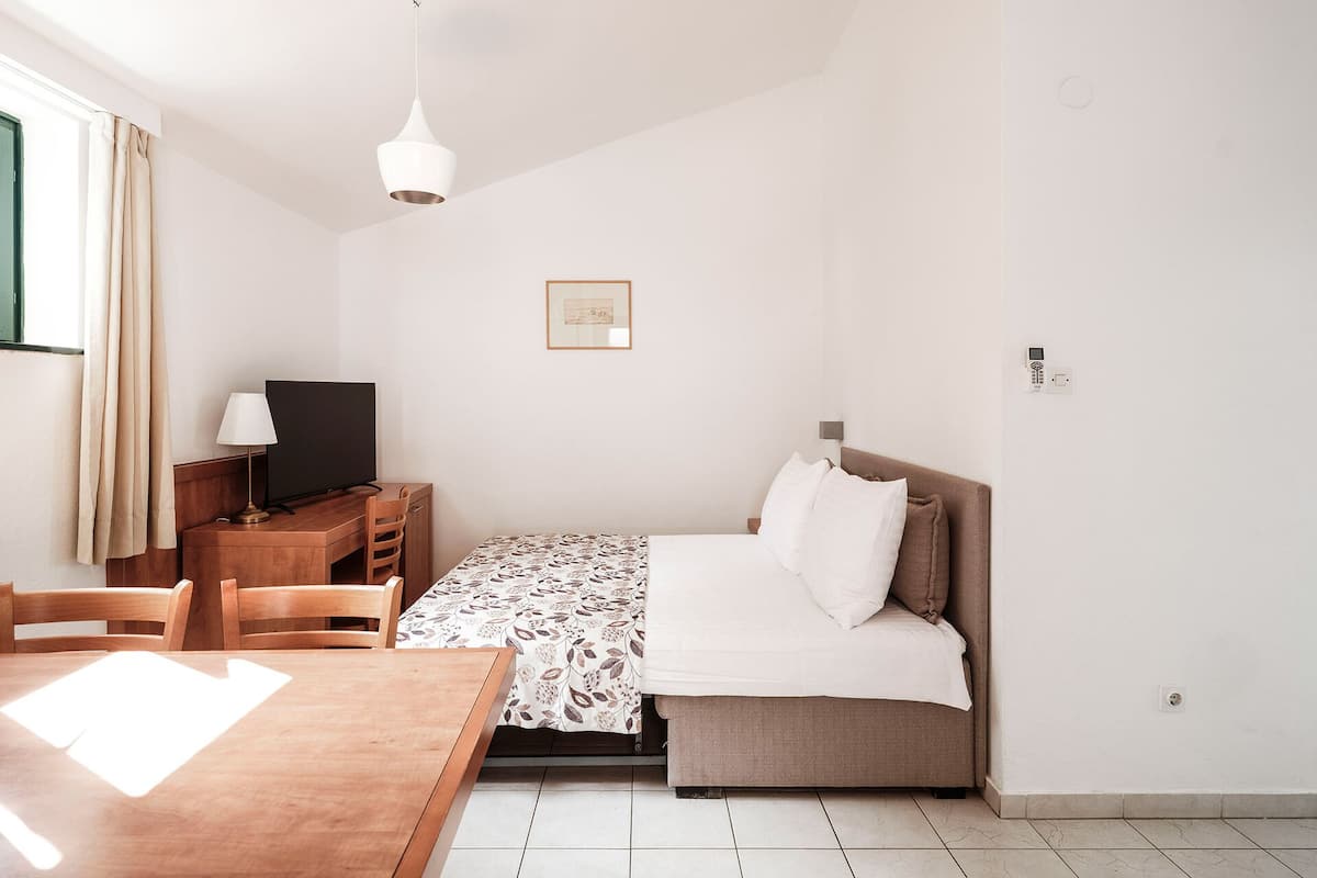 A bedroom with a bed, a desk with a chair, a TV, and a table.