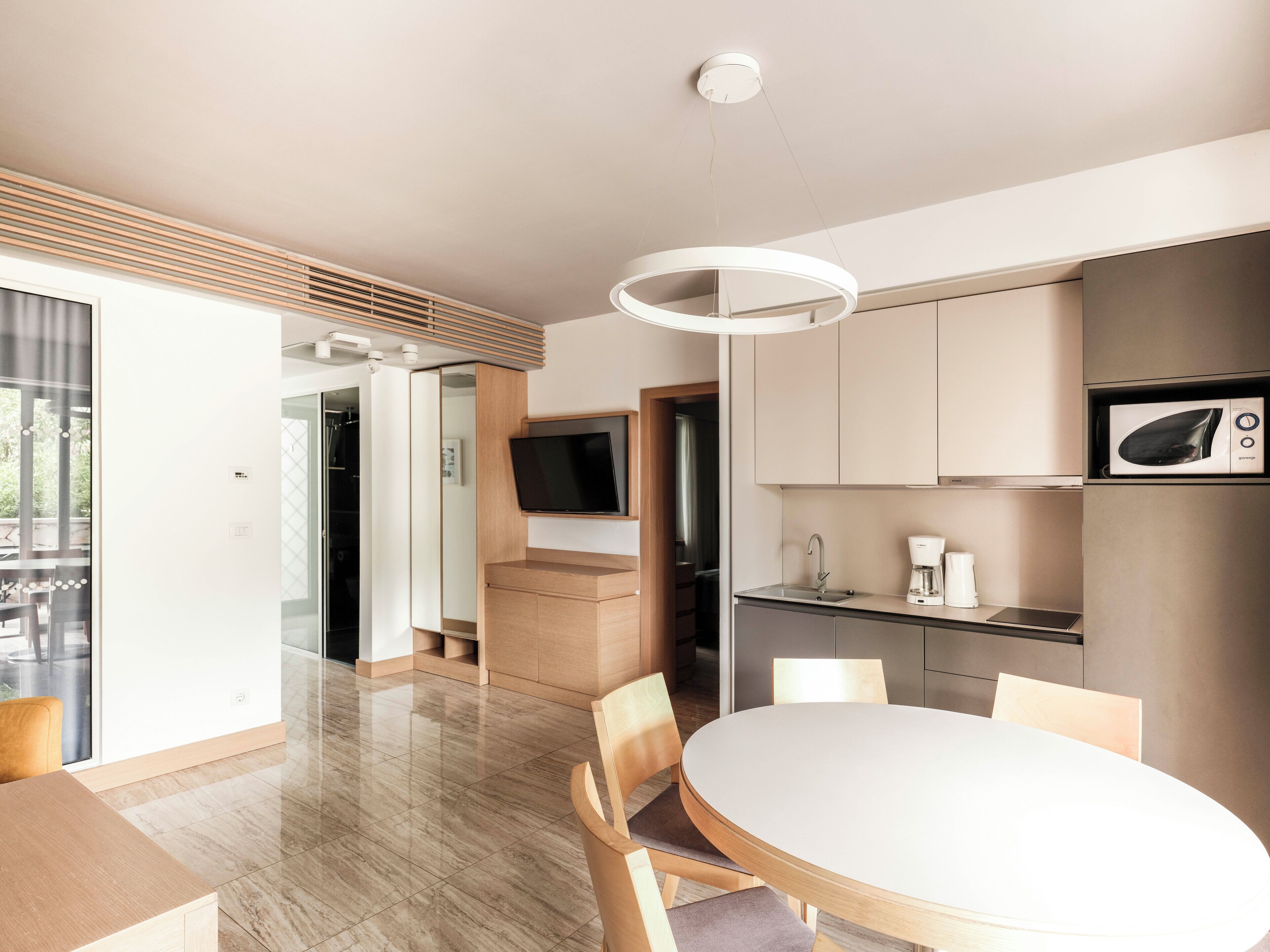 A modern kitchen with a built-in microwave, a coffee maker, and a sink. There is a dining area with a round table and chairs.