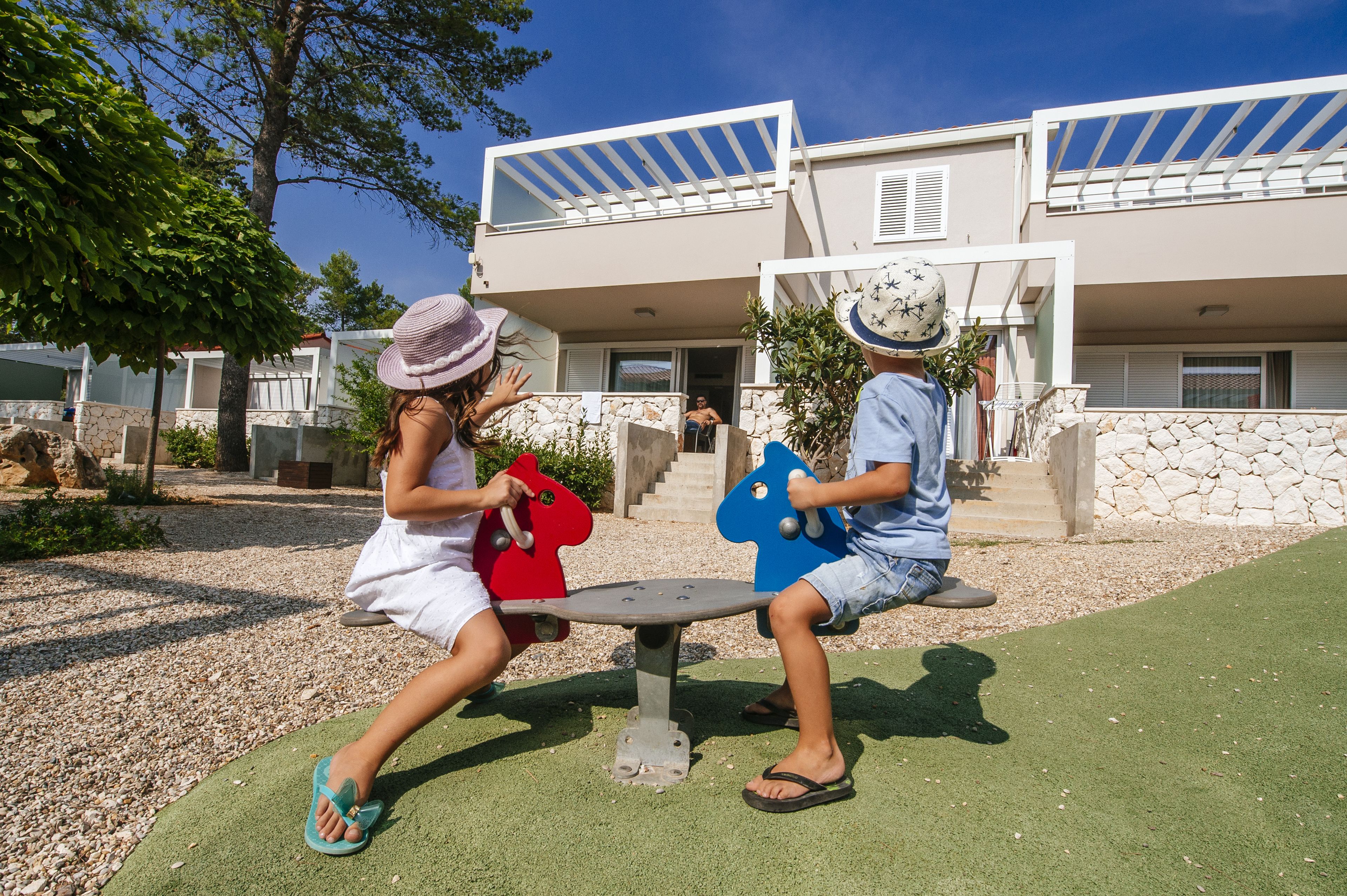 Two children playing on outdoor exercise equipment in a courtyard with a modern building in the background.